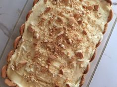 a cake with white frosting and nuts on top sitting in a glass pan, ready to be eaten