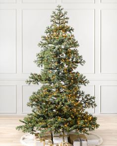 a christmas tree with presents under it on a wooden floor in front of a white wall