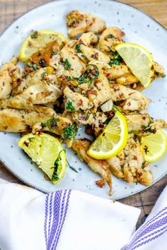 chicken with lemons and herbs on a white plate next to a blue dish towel