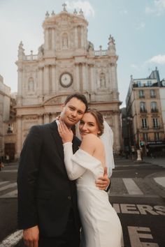 a bride and groom posing for a photo in front of a building with a clock on it