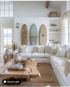 a living room filled with white furniture and surfboards hanging on the wall above it