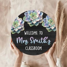 two hands holding a sign that says welcome to mrs smith's classroom with succulents