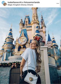 a woman standing in front of a castle wearing a minnie mouse ears headband and carrying a white purse