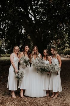 a group of women standing next to each other in front of a tree holding bouquets