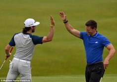 two men are high fiving each other on the golf course while one holds his hand up