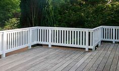 a wooden deck with white railings and trees in the background