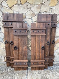 two wooden doors sitting next to each other on top of a stone wall in front of a rock wall