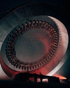 two people are sitting on a bench in front of a large circular structure that is lit up at night