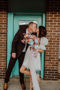 a man and woman kissing in front of a blue door with flowers on the bouquet