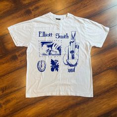 a white t - shirt with blue images on it sitting on a wooden floor next to a pair of scissors