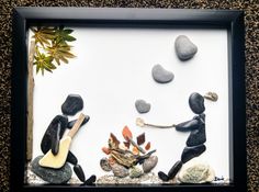 a shadow frame with some rocks and stones in it that include two people, one holding a fire