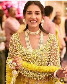 a woman in a yellow and white outfit with pearls on her head, holding flowers