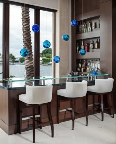 a bar with three white chairs and two blue glass balls hanging from the ceiling above it