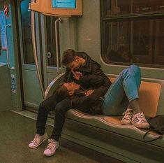 two people are sitting on a subway train and one is using his cell phone while the other looks down