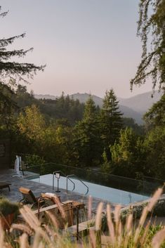 an empty swimming pool surrounded by trees and mountains in the distance with lounge chairs around it