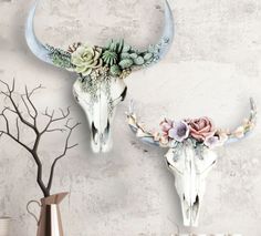 two deer skulls decorated with flowers and succulents on a wall above a shelf