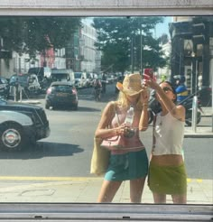 two women are standing in front of a window looking at their cell phones and taking pictures