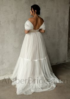 a woman in a white wedding dress standing against a wall with her back to the camera