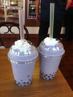 two drinks sitting on top of a wooden table next to each other with straws in them