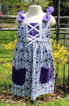 "I wish I had a model for this adorable one of a kind Summer Sundress for your little girl! This handmade dress is made of prewashed novelty cotton fabric. The main fabric is a pretty purple and lavender flower print and the coordinating accent fabric is a solid purple rose print. It is loose fitting and sleeveless with a back zipper. The bodice is fully lined and has an overlay on the front that has crisscrossed ribbon with a bow and lace at the edges. The shoulder straps have whimsical fabric bows and the full skirt has front pockets. The seams are backstitched and finished for added durability. This dress is sized for a 3 year old, but should be wearable on an older toddler based on the loose fitting design. It measures 24\" around the waist and 22\" long from shoulder to bottom of hem. Whimsical Fabric, Toddler Girl Dresses Summer, Toddler Girl Summer, Dresses For Summer, Summer Sundress, Lavender Flower, Handmade Dress, Pretty Purple, Dreamy Dress