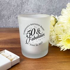 a glass with the words 50th and fabulous written on it next to some white flowers