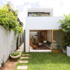 an outdoor living area with green grass and white walls, surrounded by greenery on both sides