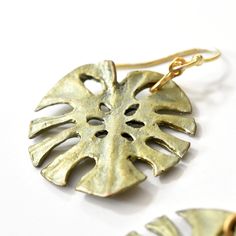 Monstera Earrings - Goldmakers Fine Jewelry Earthy Bronze Jewelry With Ear Wire, Earthy Brass Jewelry With Ear Wire, Nickel Free Green Metal Earrings, Vintage Metal Earrings, Handmade Earthy Metal Jewelry, Artisan Hand Cast Earrings As Gift, Earthy Brass Jewelry Gift, Antique Gold Hand Forged Metal Jewelry, Metal Earrings With Patina For Gift