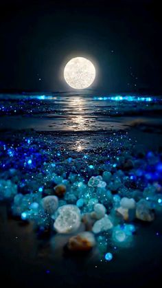 the full moon shines brightly in the night sky over water and rocks on the beach