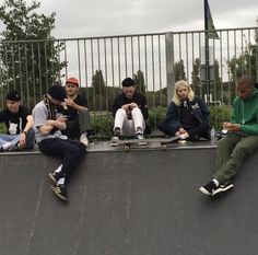 skateboarders are sitting on the edge of a ramp and looking at their phones