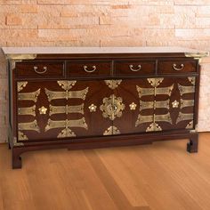 an ornately decorated chest of drawers in a room with wood flooring and brick wall