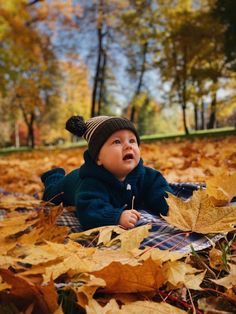 a baby is laying on the ground with leaves in front of him and looking up