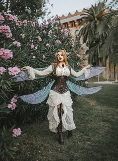 a woman dressed as a fairy standing in front of flowers