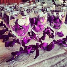 there are many wine glasses that have purple decorations in them and ribbons on the table