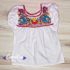 Cute Girl Mexican Puebla blouse made of 100% Cotton poplin fabric. Embroidered frontal detail in silk thread. Shop our entire Puebla Collection here. AGE SHOULDER TO SHOULDER BUST 1 9" 20" 2 10" 21" 4 11" 24" 6 12" 26" 8 13" 28" 10 14" 30" 12 15" 32" 14 16" 34" Measurements are approximate sizes. Lengths may vary by 1-2 inches. CARE:• Cold wash, delicate, inside out. • Hang dry.• Do not machine dry. MADE IN OAXACA, MEXICO Each design and color is unique to each blouse as they are made by differe Festive White Top With Embroidered Sleeves, Traditional Cotton Peasant Top With Embroidered Hem, Embroidered Multicolor Blouse For Traditional Ceremonies, Traditional Peasant Top With Embroidered Hem For Festival, Traditional White Embroidered Peasant Top, Traditional White Peasant Top With Embroidered Neckline, Traditional Cotton Top With Embroidered Sleeves, White Traditional Peasant Top With Floral Embroidery, Traditional White Peasant Top With Floral Embroidery