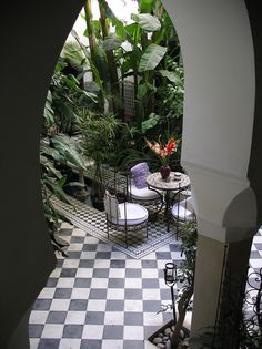 an outdoor patio with potted plants and tables in the center is seen through an archway