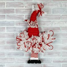 a red and white christmas decoration hanging on a brick wall with the word santa spelled in cursive letters