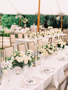 a long table with white flowers and greenery is set up for an outdoor wedding reception