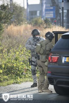 two police officers standing next to each other near a car on the side of the road