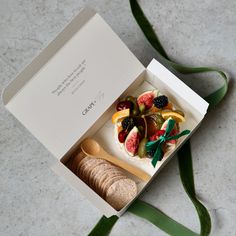 a box filled with fruit and crackers on top of a table next to a green ribbon