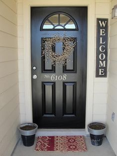 a black front door with welcome sign and two flower pots