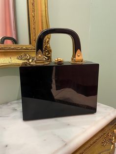 D E S C R I P T I O N Vintage 1950s black acrylic box bag with gold tone hardware. minor fading on handles. M E A S U R E M E N T S Bag Length: 8" Bag Width: 3.5" taken from the sides Bag Height: 6" excluding shoulder strap Bag strap drop: 4" top handle, Authenticity Guarantee All bags sold in our shop are 100% guaranteed authentic or your money back. Luxury Vintage Square Box Bag, Black Box Bag For Shopping, Vintage Rectangular Box Bag For Party, Vintage Rectangular Box Bag For Shopping, Retro Rectangular Evening Box Bag, Retro Rectangular Box Bag For Evenings, Vintage Formal Box Bag With Gold-tone Hardware, Vintage Rectangular Box Bag For Gift, Formal Square Box Bag With Original Box