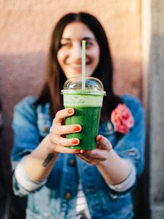 a woman holding up a green smoothie in her hand