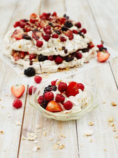 two desserts with strawberries, berries and cream on them sitting on a wooden table