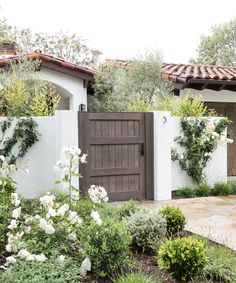 a garden with white flowers and greenery in front of a house that has a wooden door