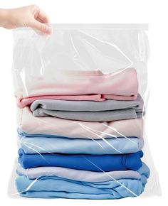 a hand is holding a plastic bag full of folded shirts and t - shirts on top of each other