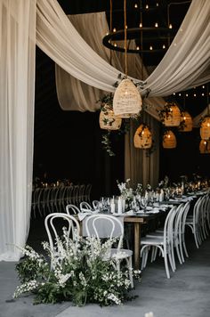 a long table with white chairs and greenery on the top is surrounded by hanging chandeliers