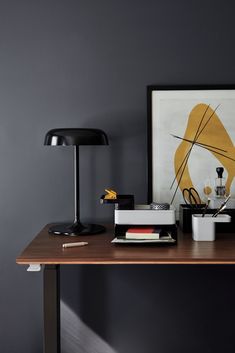 a desk with a lamp, books and other items on it in front of a gray wall