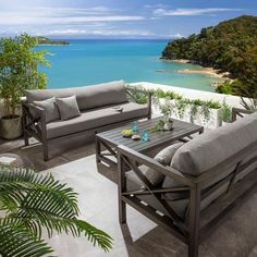 an outdoor seating area overlooking the ocean and beach with tropical plants in vases on table