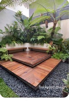 a wooden deck surrounded by greenery and plants in a backyard area with black gravel