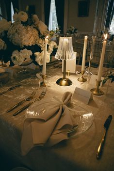 the table is set with silverware and white flowers in vases, candles, and napkins